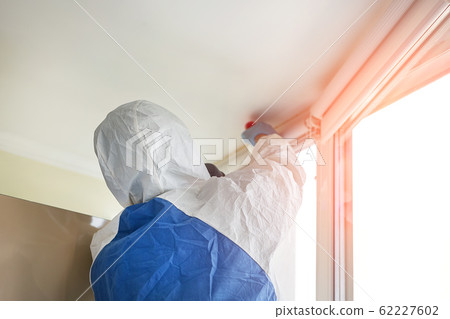 Man wearing protective biological suit and gas-mask due to mers coronavirus global pandemic warning and danger. Worker make disinfection, pest control and mold removal and ventilation at house room 62227602