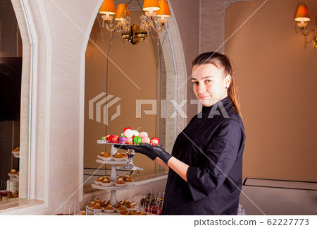 The waiter serves a stand of colorful macaroons at sweet table. 62227773