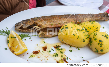 Fresh Hallstatt trout and potatoes recipe on the white dish at Hallstatter See or Lake Hallstatt, a lake in the Salzkammergut, Austria Fresh Hallstatt trout and potatoes recipe on the white dish at Hallstatter See or Lake Hallstatt, a lake in the Salzkammergut, Austria 62228432