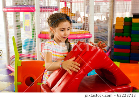 Little cute girl builds house with soft big blocks at indoor playground 62228718