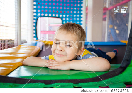 Cute little boy resting on colorful playground trampoline Cute little boy resting on colorful playground trampoline 62228738