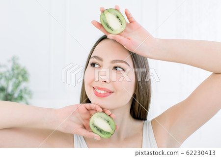 Beauty smiling woman and slices of Kiwi fruit - The woman is dieting healthy isolated on the light background, Caucasian female 62230413