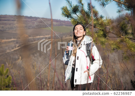 woman hiking a hill stopped for a drink. woman traveler drinking tea from a thermos on hill woman hiking a hill stopped for a drink. woman traveler drinking tea from a thermos on hill 62236987
