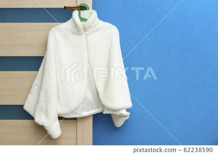 Fashionable white female coat hanging on door handle on blue wall background Fashionable white female coat hanging on door handle on blue wall background 62238590