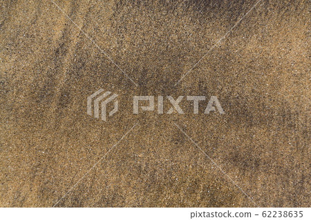 Waves coming and leaving wet sand on sea shore, brown yellow and black grains from volcanic ash, zen background, harmony and meditation concept, flat lay top view, copy space 62238635