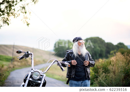 Senior man traveller with motorbike and sunglasses in countryside. Senior man traveller with motorbike and sunglasses in countryside. 62239316