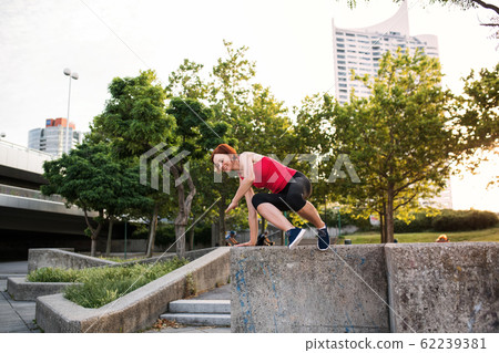 Young sportswoman outdoors in city, jumping from concrete wall. Young sportswoman outdoors in city, jumping from concrete wall. 62239381
