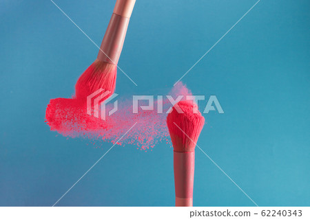 close-up photo of two professional make-up brushes with pink powder in motion on blue background 62240343