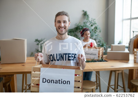 Young volunteer standing in room with a charity box. Young volunteer standing in room with a charity box. 62253762
