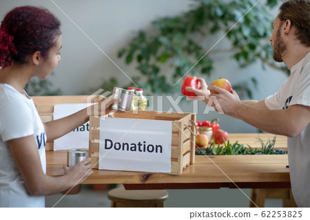 Young girl, man volunteers packing food box for those in need. 62253825