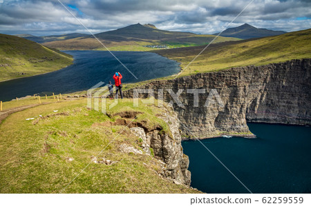 Tourists over Sorvagsvatn lake cliffs over the ocean under the clouds, Faroe Islands 62259559