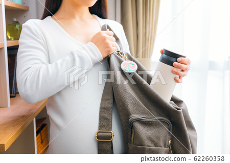 Pregnant woman putting a water bottle in a backpack 62260358