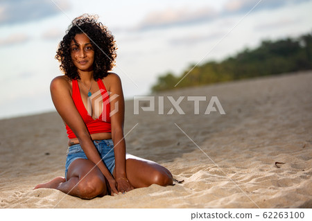 Dark-skinned girlfriend sitting on the beach in the evening 62263100