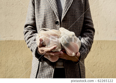 man carrying mesh bags full of fruit and vegs. 62265122