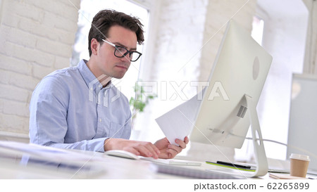 Working Young Man Reading Documents in Office 62265899