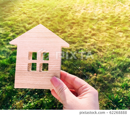 Miniature wooden house on green grass in female hands. Real estate concept. Modern housing. Eco-friendly and energy efficient house. Buying a home outside the city. Nature. Fresh air. Mortgage, loan. Miniature wooden house on green grass in female hands. Real estate concept. Modern housing. Eco-friendly and energy efficient house. Buying a home outside the city. Nature. Fresh air. Mortgage, loan. 62268888