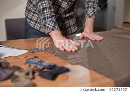 Close-up hands of Tailor, cutting wool fabric. Craftsman Makes rectangular blanks for Bow ties of woolen fabric. Work with sewing machine in a textile studio. Close-up hands of Tailor, cutting wool fabric. Craftsman Makes rectangular blanks for Bow ties of woolen fabric. Work with sewing machine in a textile studio. 62271567