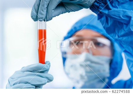 Medic in hazmat protective suit holds a test tube with a coronavirus positive blood sample from Wuhan, China. 2019 nCoV pandemic. stop coronavirus. MERS. Medic in hazmat protective suit holds a test tube with a coronavirus positive blood sample from Wuhan, China. 2019 nCoV pandemic. stop coronavirus. MERS. 62274588