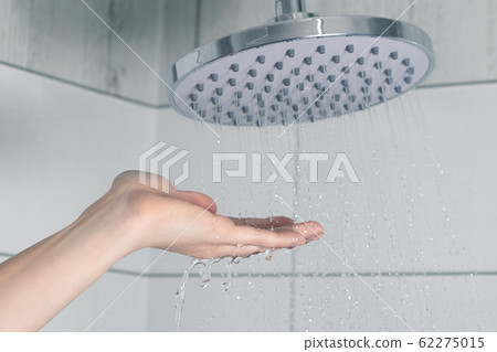 Female hand touching water pouring from a rain shower head, checking water temperature 62275015