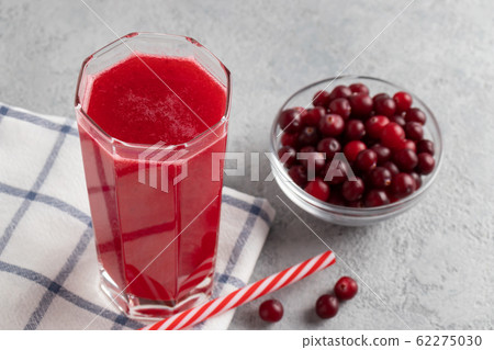One glass with homemade freshly cranberry juice and a bowl of cranberries on a gray concrete table One glass with homemade freshly cranberry juice and a bowl of cranberries on a gray concrete table 62275030