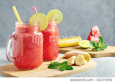 Watermelon smoothie with banana, lime and mint in mug jars on a cutting board. Healthy eating concept Watermelon smoothie with banana, lime and mint in mug jars on a cutting board. Healthy eating concept 62275092