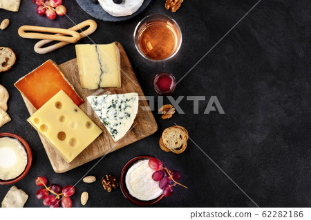 Cheese platter, shot from the top on a black background with copy space. Blue cheese, Brie, Dutch cheese and others with wine 62282186