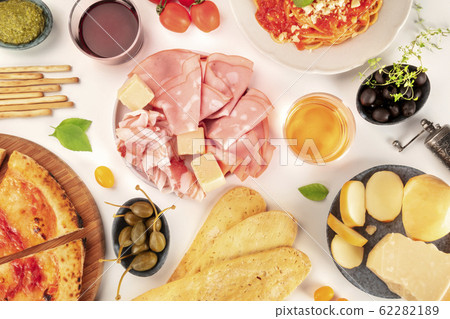 Italian food, flat lay overhead shot. Pizza, pasta, cheese, ham, wine, olives, pesto, shot from above on a white background 62282189