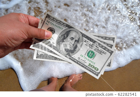 Girl holding money bill of 300 dollars on background of sea ocean waves Girl holding money bill of 300 dollars on background of sea ocean waves 62282541