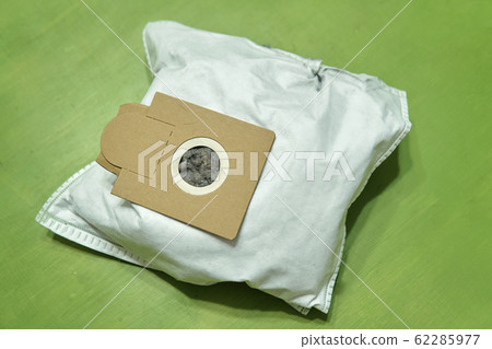 Used dust bag full of a dirt and garbage lying on the green surface close up 62285977