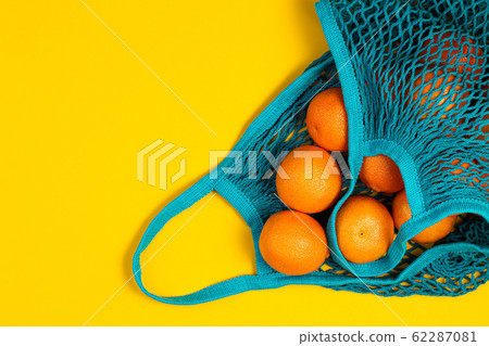 Tangerines in green color string bag on yellow 62287081