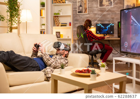Man gamer using a VR headset to play video games in the living room Man gamer using a VR headset to play video games in the living room 62288637