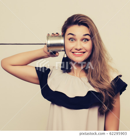 portrait of young woman hearing through a tin can 62295903