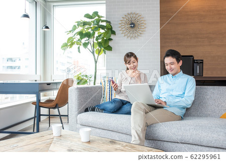 Young couple talking while looking into a personal computer in the living room Young couple talking while looking into a personal computer in the living room 62295961