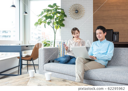 Young couple talking while looking into a personal computer in the living room Young couple talking while looking into a personal computer in the living room 62295962