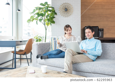 Young couple talking while looking into a personal computer in the living room Young couple talking while looking into a personal computer in the living room 62295963