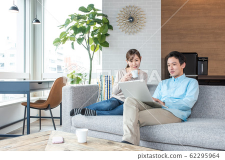 Young couple talking while looking into a personal computer in the living room Young couple talking while looking into a personal computer in the living room 62295964