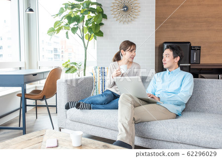Young couple talking while looking into a personal computer in the living room Young couple talking while looking into a personal computer in the living room 62296029