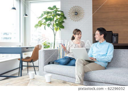 Young couple talking while looking into a personal computer in the living room Young couple talking while looking into a personal computer in the living room 62296032
