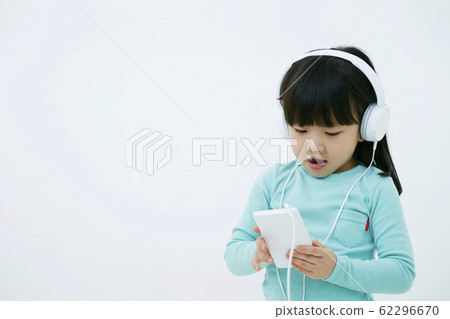 在智能手機的女孩聽的音樂有在白色背景隔絕的耳機的 在智能手機的女孩聽的音樂有在白色背景隔絕的耳機的 62296670