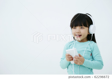 在智能手機的女孩聽的音樂有在白色背景隔絕的耳機的 在智能手機的女孩聽的音樂有在白色背景隔絕的耳機的 62296672