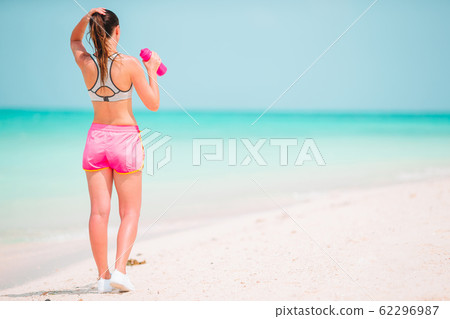 Fit young woman doing exercises on tropical white beach in her sportswear 62296987