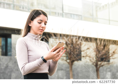 attractive business woman holding mobile phone seeking information on internet in front of business center 62297730