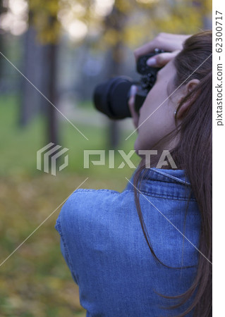 A woman takes pictures on a black compact camera against the background of a beautiful autumn park A woman takes pictures on a black compact camera against the background of a beautiful autumn park 62300717