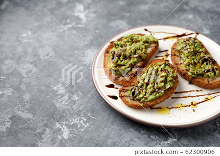 A freshly made minced avocado toast with balsamico dressing, linseed or flaxseed and oil on a white plate, on a gray background with a copyspace 62300906