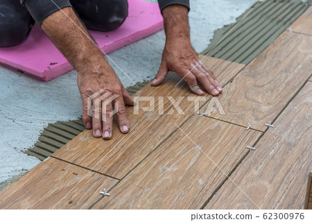 Worker placing ceramic floor tiles on adhesive 62300976