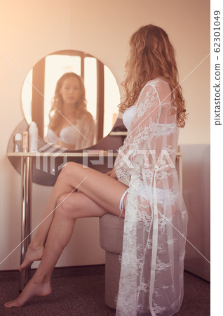 Beautiful young woman in white lace peignoir sits 62301049