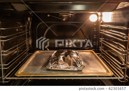 Food covered with foil on the pan inside oven Food covered with foil on the pan inside oven 62301657