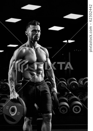 Monochrome portrait of bodybuilder carrying weights. 62302442