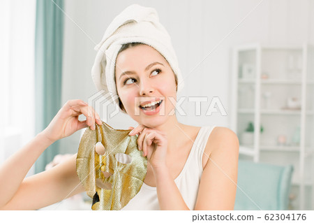 Cosmetic procedure, pretty funny girl in white towel with gold sheet mask on light background. Beauty, spa, skin and body care. Cosmetic procedure, pretty funny girl in white towel with gold sheet mask on light background. Beauty, spa, skin and body care. 62304176