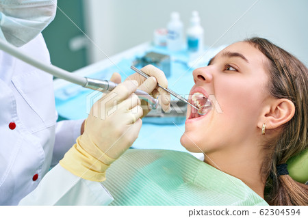 Girl sitting at dental chair with open mouth during oral check up while doctor. Visiting dentist office. Dentistry concept. Girl sitting at dental chair with open mouth during oral check up while doctor. Visiting dentist office. Dentistry concept. 62304594